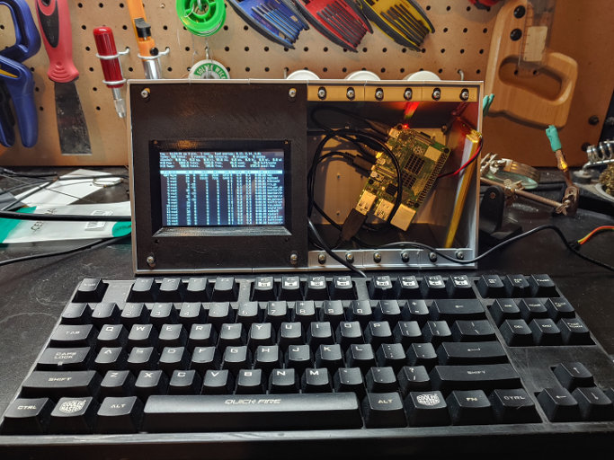 A silver box with a computer screen mounted into a black panel on one side. The other side is open, with a circuit board and battery sitting in it.