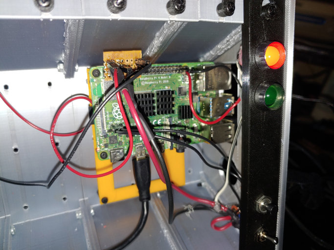 A close up of a circuit board with a smaller board and wires plugged into it. LEDs and switches are mounted in a nearby black panel.