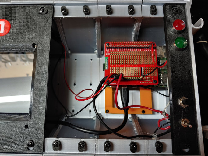 The smaller board from before has been replaced with a red board the same size as the one it's plugged into. There are multiple rows of headers on it, with wires plugged into some of them.