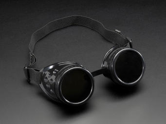 Plastic costume goggles in the style of Victorian welding goggles: Cylindrical eye cups with flat lenses, attached by a strip across the bridge of the nose, and held on with an elastic band.