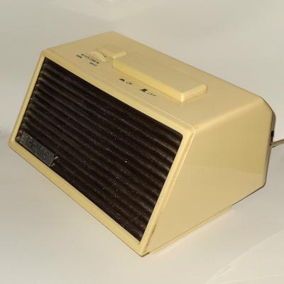 An off-white plastic speaker with a brown plastic grill. There are two buttons and a sideways volume knob on the top. A silver badge on the front reads 'TeleMate'.