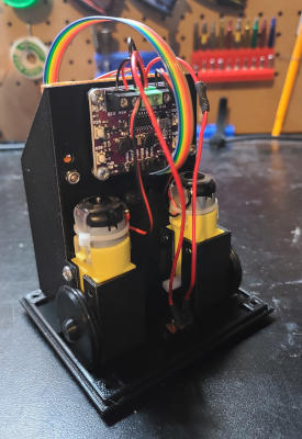 A black plastic frame with a flat bottom and a vertical partition in the center. Motors and a circuit board are mounteted against the partition.